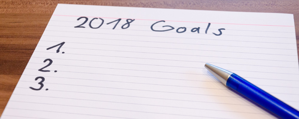 Lined white notecard titled 2018 Goals and numbered one, two, and three with a blue pen sitting on top